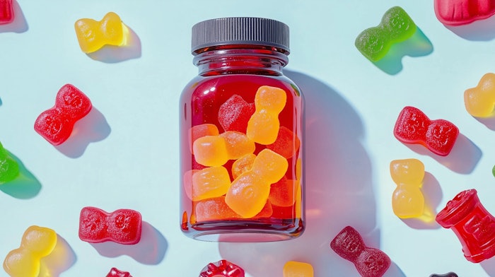 A bottle of colorful gummy chewable supplements surrounded by scattered gummies on a light blue background.