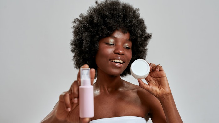 Black woman curly hair holding lotion and cream products