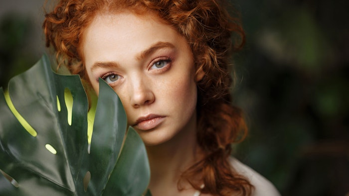 beautiful redhead holding jungle foliage near face
