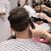 Client receiving a haircut from a barber in a barbershop/salon.