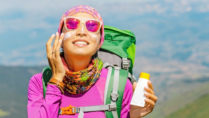 woman hiking mountains backpack using sunscreen