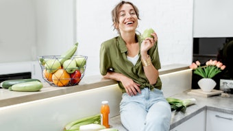 Portrait of a young and cheerful woman with healthy raw food on the kitchen at home. Vegetarianism, wellbeing and healthy lifestyle concept