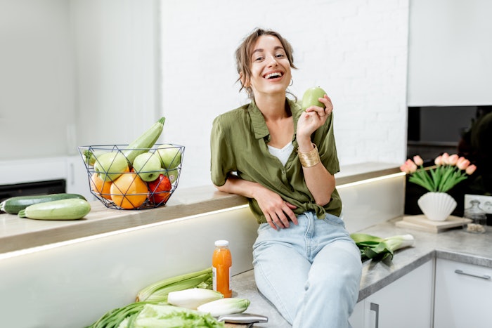 Portrait of a young and cheerful woman with healthy raw food on the kitchen at home. Vegetarianism, wellbeing and healthy lifestyle concept
