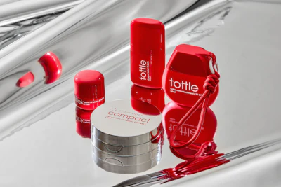 Red and white cosmetic product collection including bottles, containers, and applicators arranged on reflective surface