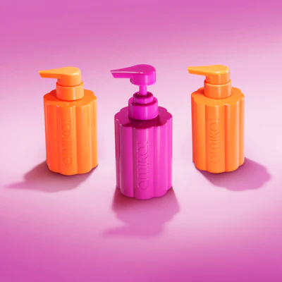 Three cosmetic pump bottles in orange and magenta colors on a pink gradient background