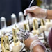 Factory workers assembling or inspecting bottled products on an industrial production line with metal components and equipment.
