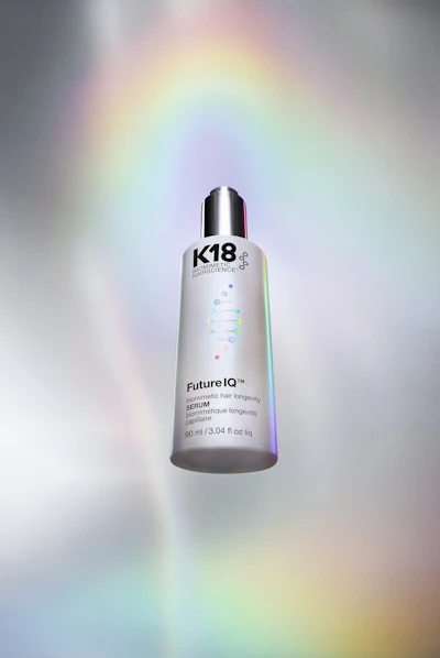 K18 Future IQ hair longevity serum bottle, 90ml, displayed against iridescent gradient background