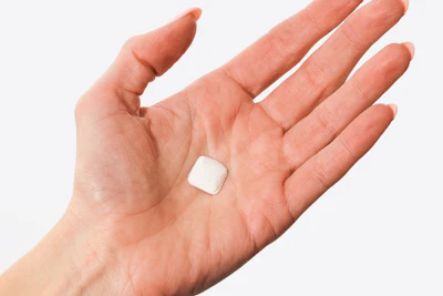 Small white square tablet or medication held in an open palm against white background