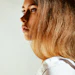 Woman with long caramel-blonde hair in profile wearing white shirt against neutral background
