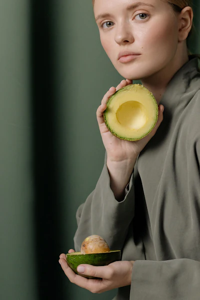 Woman in sage green shirt holding fresh halved avocados against green background