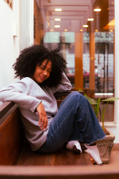 Woman with natural curly hair smiling while sitting in a modern corridor with warm lighting