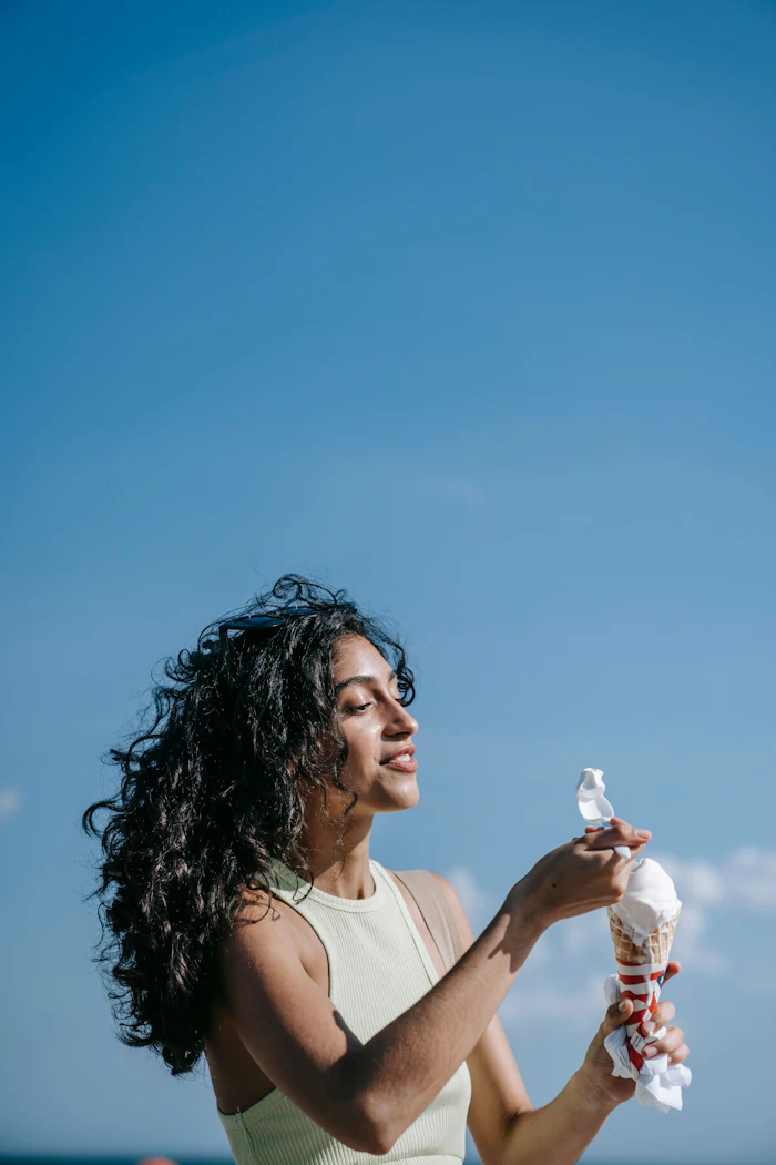 Woman in cream tank top holding beverage bottles outdoors against clear blue sky