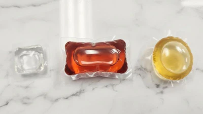 Three laundry detergent pods in clear, red, and yellow on white marble surface