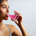 Young woman drinking pink beverage from striped cup against neutral background