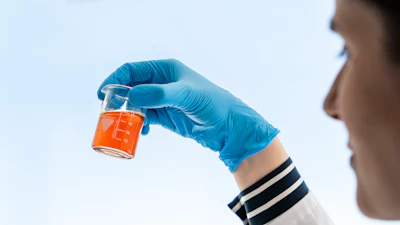 Scientist in blue gloves holding beaker with orange liquid solution