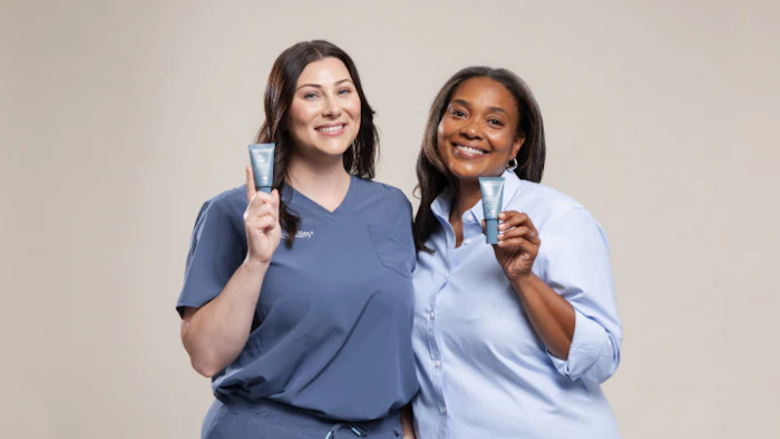 Two smiling women in professional attire posing together against a neutral beige background