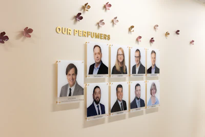 Team wall display titled 'Our Perfumers' featuring nine professional headshots of perfume company employees with decorative floral accents
