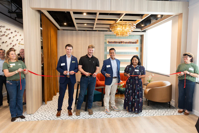 Group of professionals holding red ribbon at indoor ribbon-cutting ceremony in modern office space