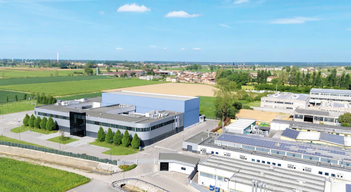 Aerial view of modern industrial facility with blue-roofed building, manufacturing structures, and surrounding agricultural fields