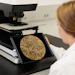 Scientist viewing microplate reader displaying golden crystalline sample analysis on monitor