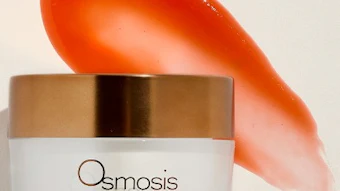 Osmosis Apple Spice skincare cream in glass jar with gold lid and coral-colored product swatch