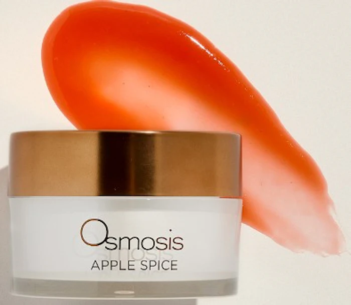 Osmosis Apple Spice skincare cream in glass jar with gold lid and coral-colored product swatch