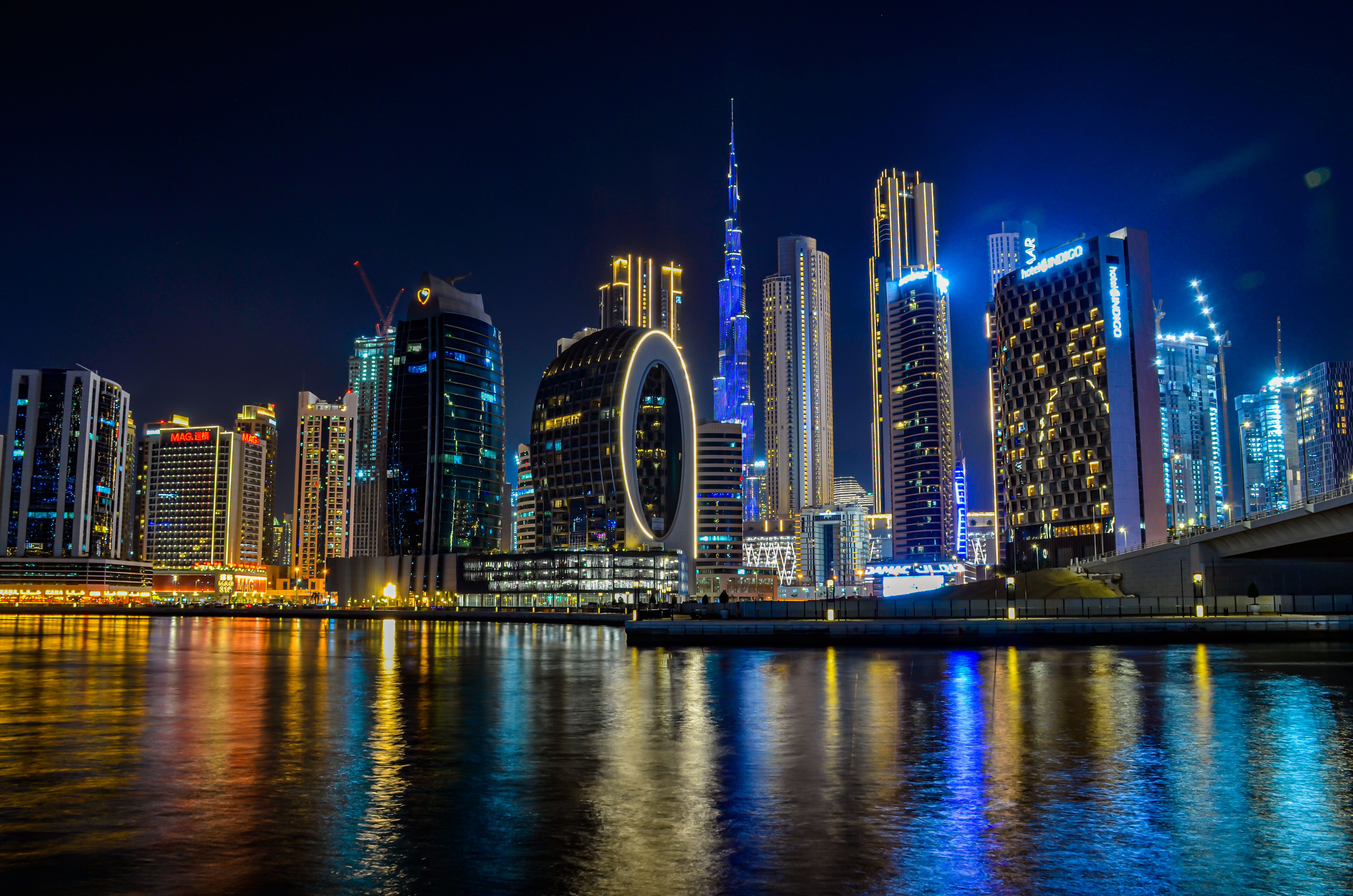 Dubai downtown skyline at night with illuminated skyscrapers and glowing Ferris wheel reflected in calm waterfront