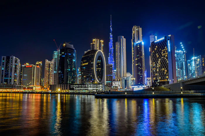 Dubai downtown skyline at night with illuminated skyscrapers and glowing Ferris wheel reflected in calm waterfront