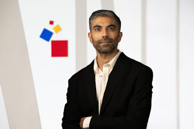 Professional man in black blazer and white shirt standing against white wall with geometric shapes