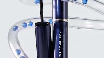 Revitalash Peptide Complex eyeliner with brush displayed among clear decorative tubes filled with blue spheres