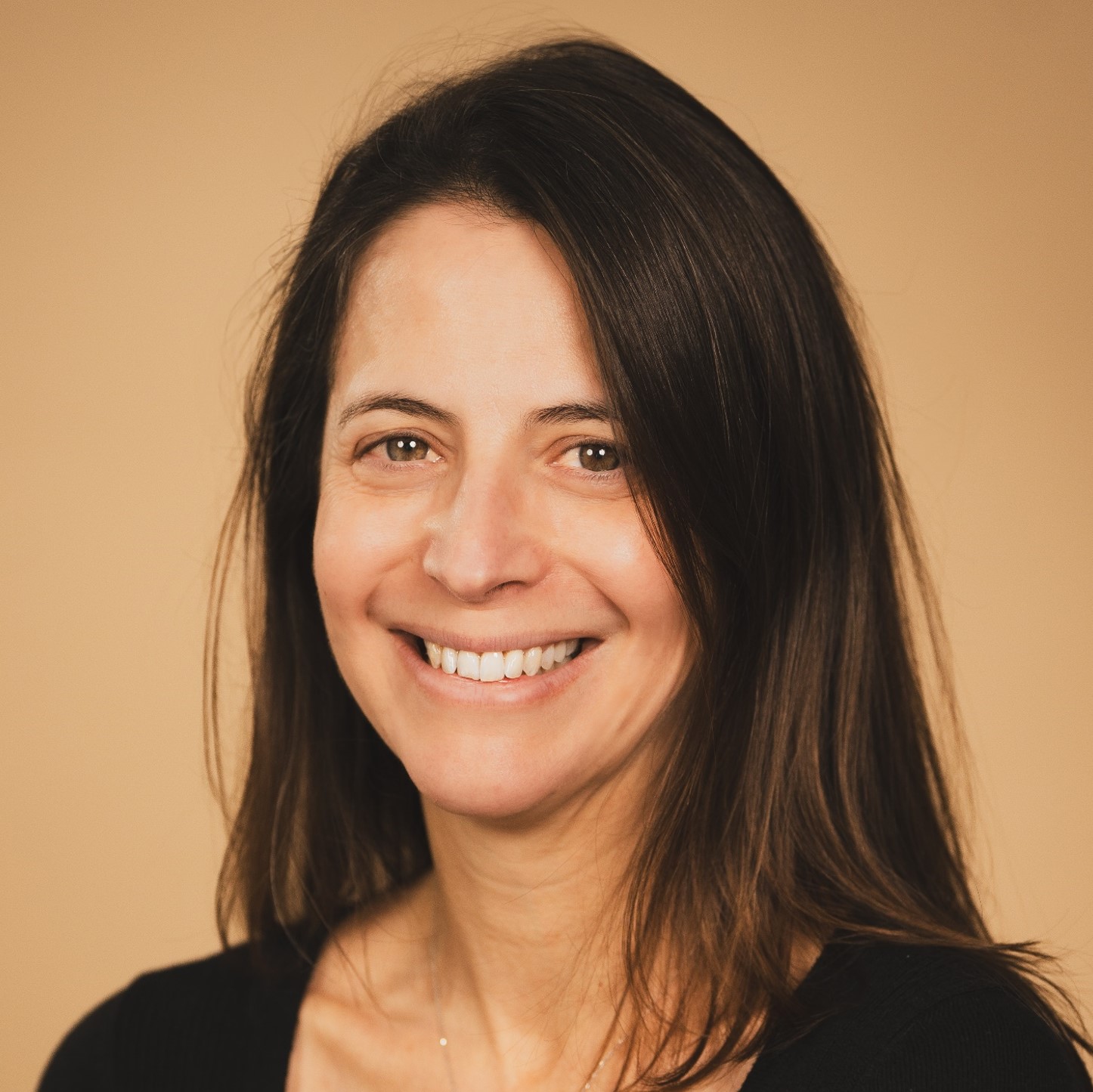 Professional headshot of a woman with long dark hair smiling against a tan background
