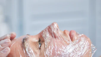 Person's face covered in clear plastic wrap showing skincare treatment or cosmetic application