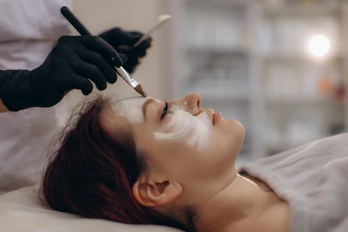 Esthetician applying white facial mask to client during professional skincare treatment