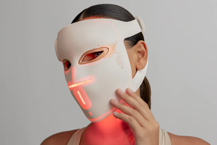 Person wearing white LED light therapy mask with red illuminated accents on face and chin area