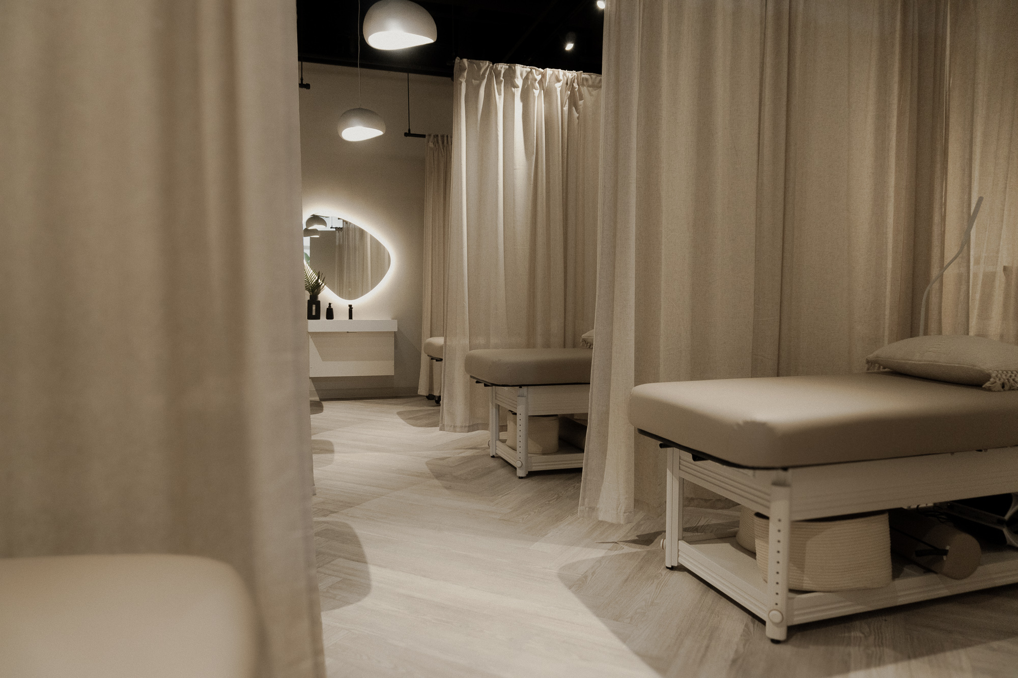 Modern spa treatment room with cream-colored massage beds, curtain partitions, and ambient lighting fixtures