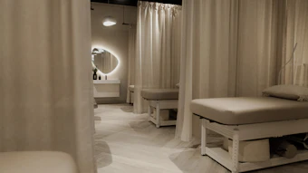 Modern spa treatment room with cream-colored massage beds, curtain partitions, and ambient lighting fixtures