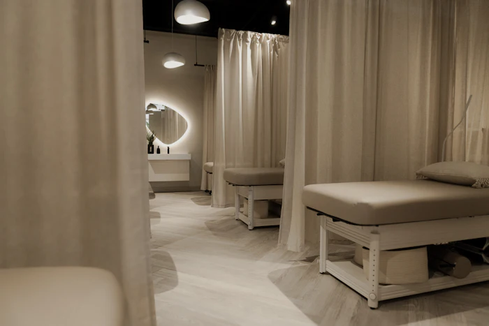 Modern spa treatment room with cream-colored massage beds, curtain partitions, and ambient lighting fixtures