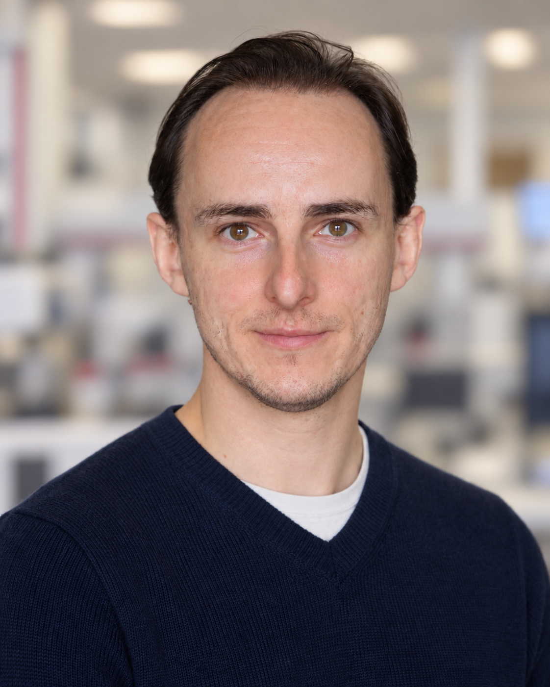Professional headshot of a man with dark hair wearing a navy sweater in an office setting