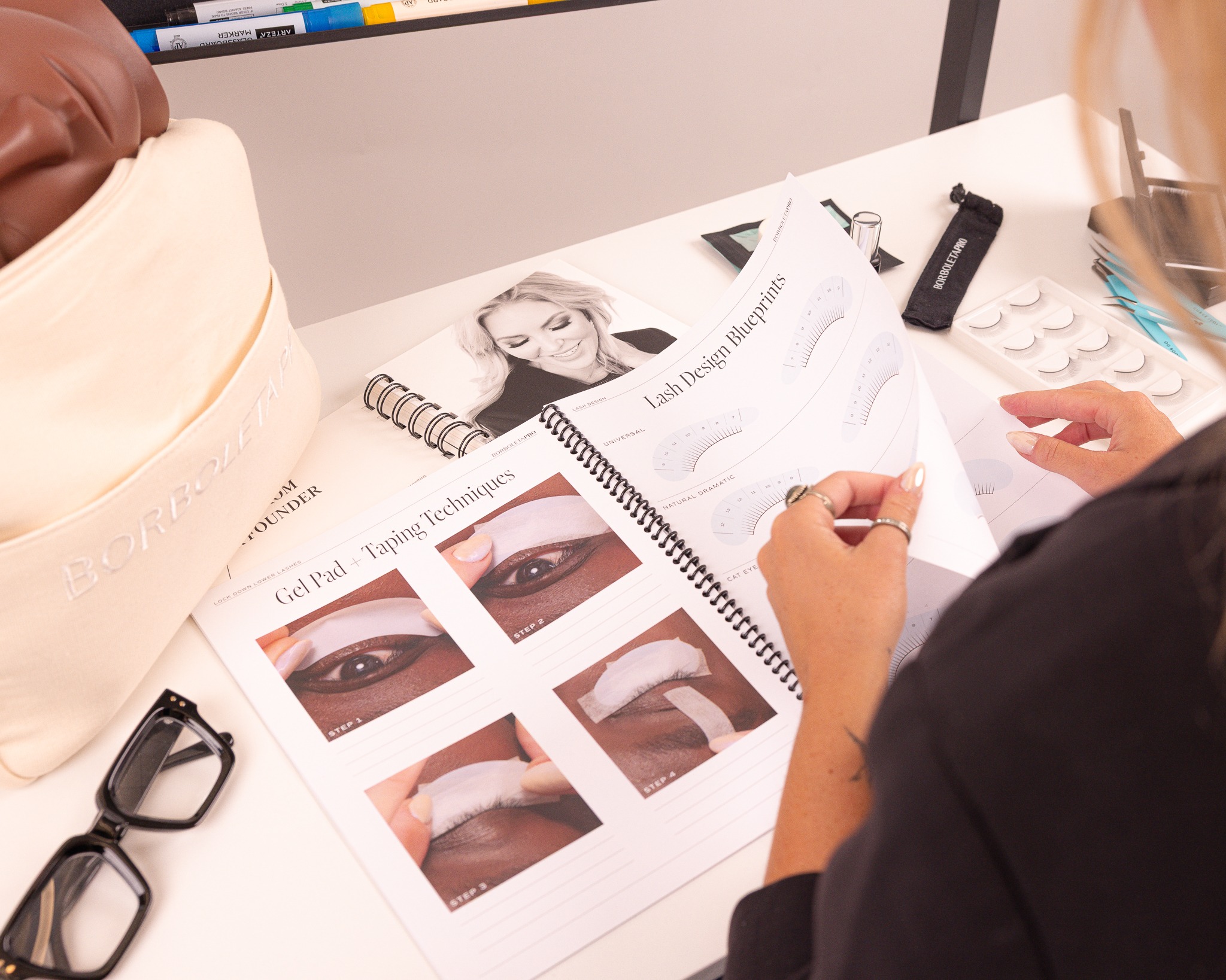 Makeup artist reviewing eye makeup tutorial guide with technique demonstrations and beauty products on desk