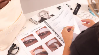 Makeup artist reviewing eye makeup tutorial guide with technique demonstrations and beauty products on desk