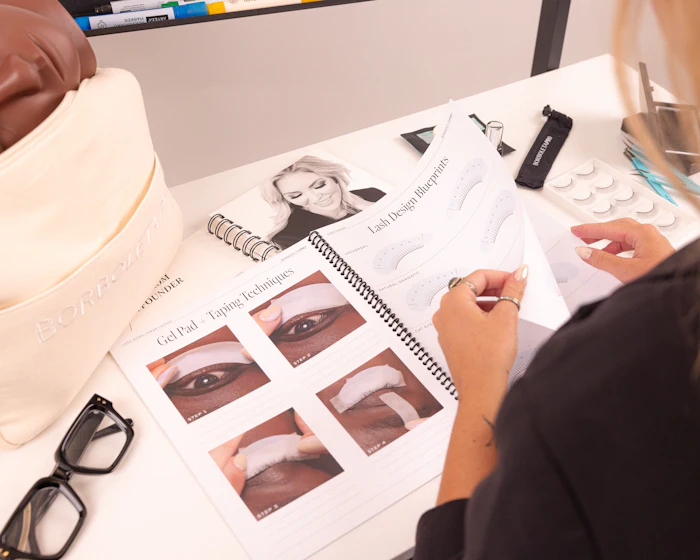 Makeup artist reviewing eye makeup tutorial guide with technique demonstrations and beauty products on desk