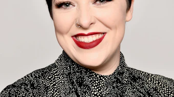 Professional headshot of a woman with short black hair, red lipstick, wearing a black and white patterned jacket against a neutral background