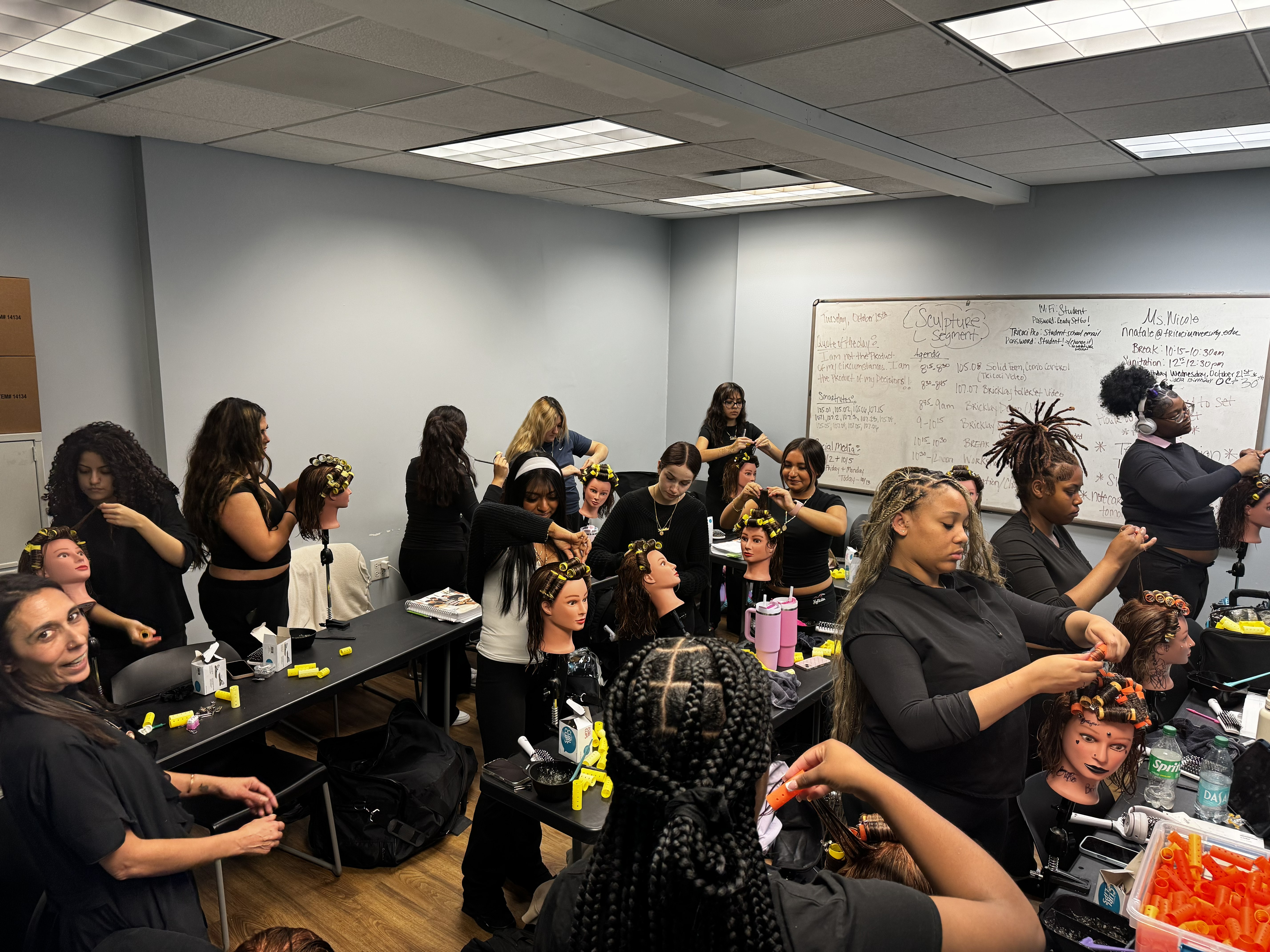 Group of women participating in a hair braiding workshop in a classroom with whiteboards and supplies