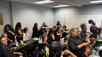 Group of women participating in a hair braiding workshop in a classroom with whiteboards and supplies