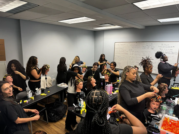 Group of women participating in a hair braiding workshop in a classroom with whiteboards and supplies
