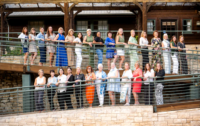 Large group of women posed together on a two-level wooden deck with metal railings at a rustic venue
